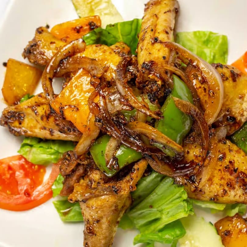 Vietnamese chicken wings with onions, green peppers, and a side salad on a white plate.