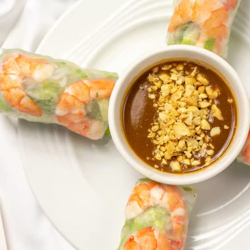Vietnamese shrimp spring rolls with a side of peanut dipping sauce, garnished with crushed peanuts.
