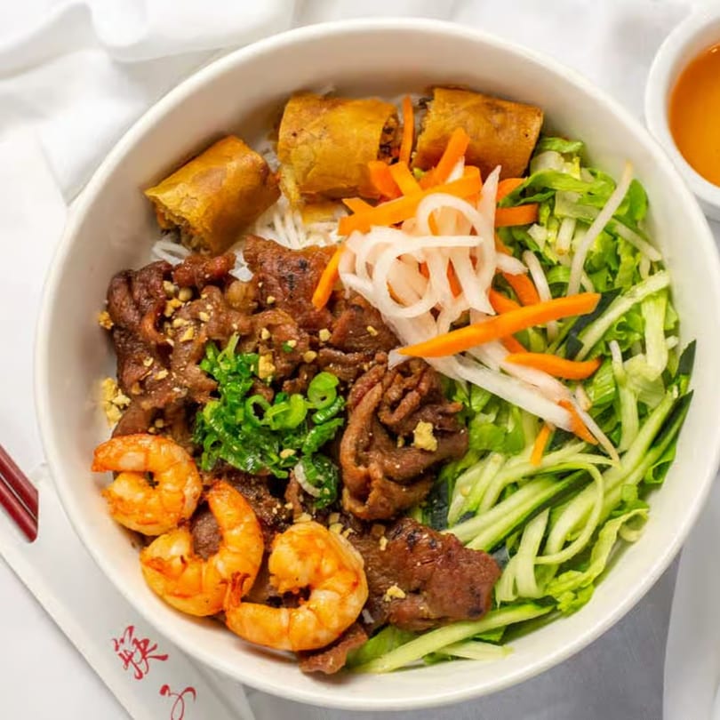 Vietnamese vermicelli bowl with grilled beef, shrimp, crispy spring rolls, and fresh vegetables.